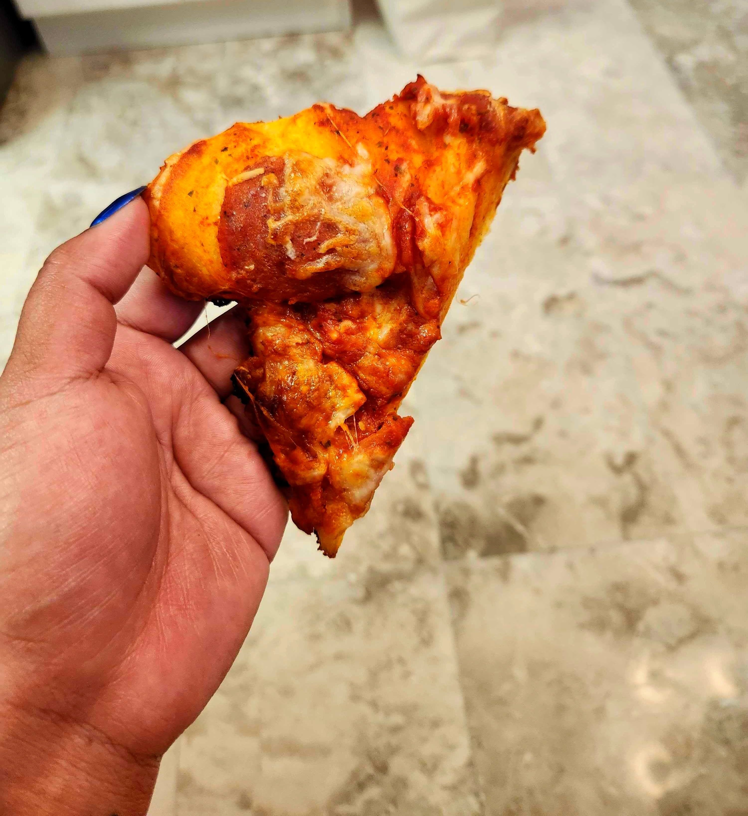 A hand with blue nails holding a slice of pizza against a tile background.