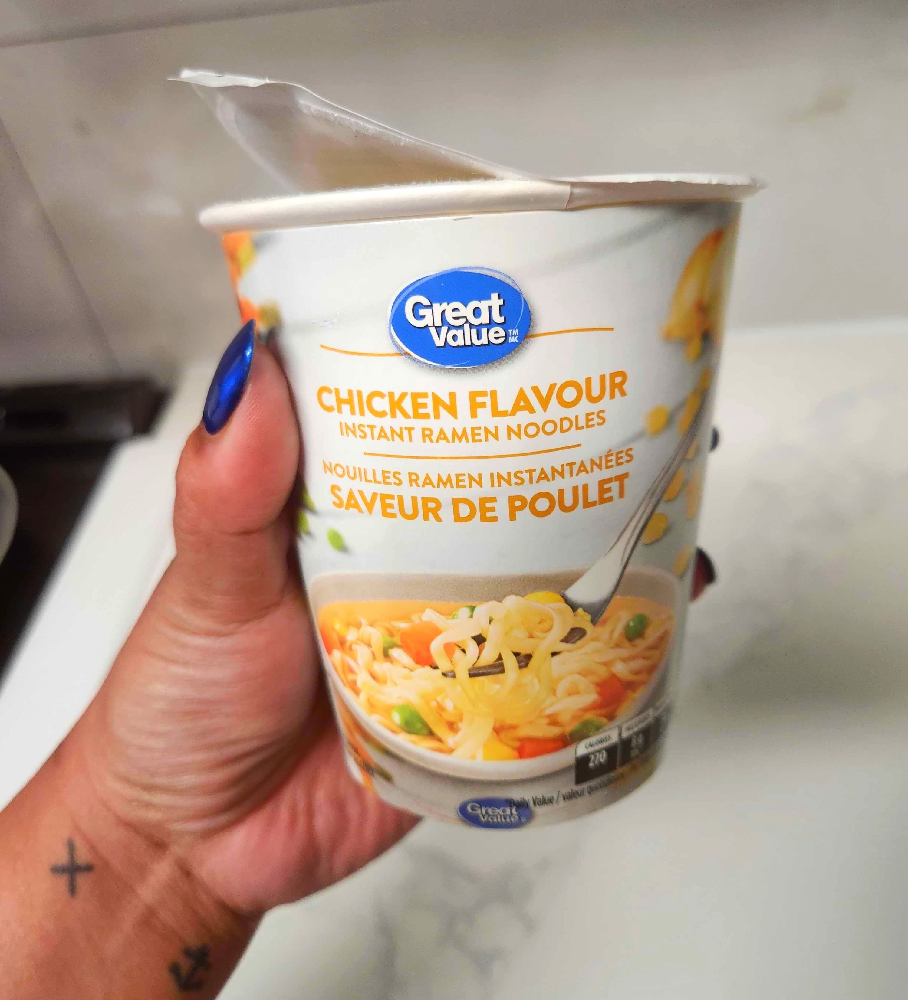 A hand with blue nails holding a white container of soup against a marble counter.