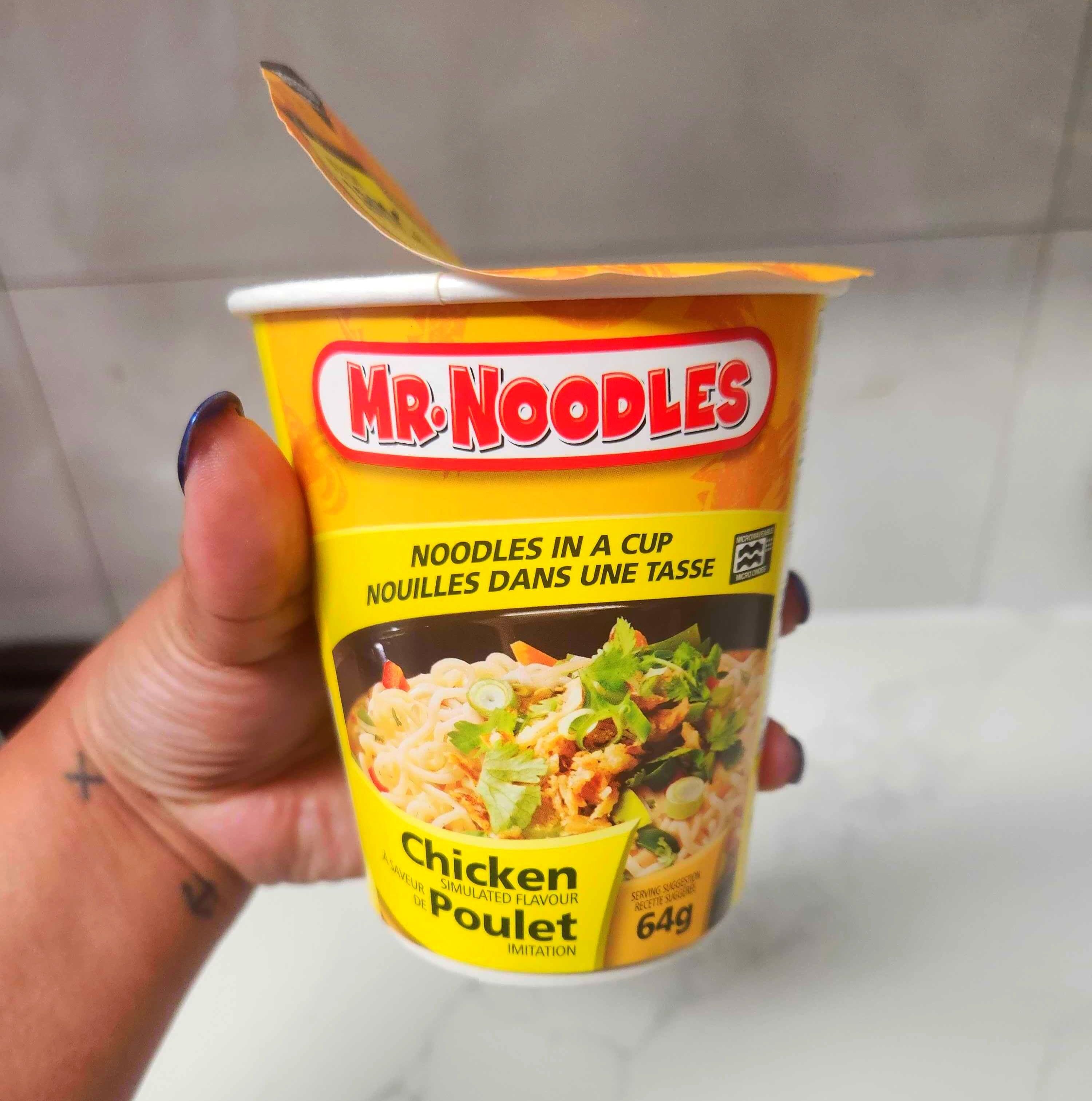 A hand with blue nails holding a yellow container of soup against a marble counter.
