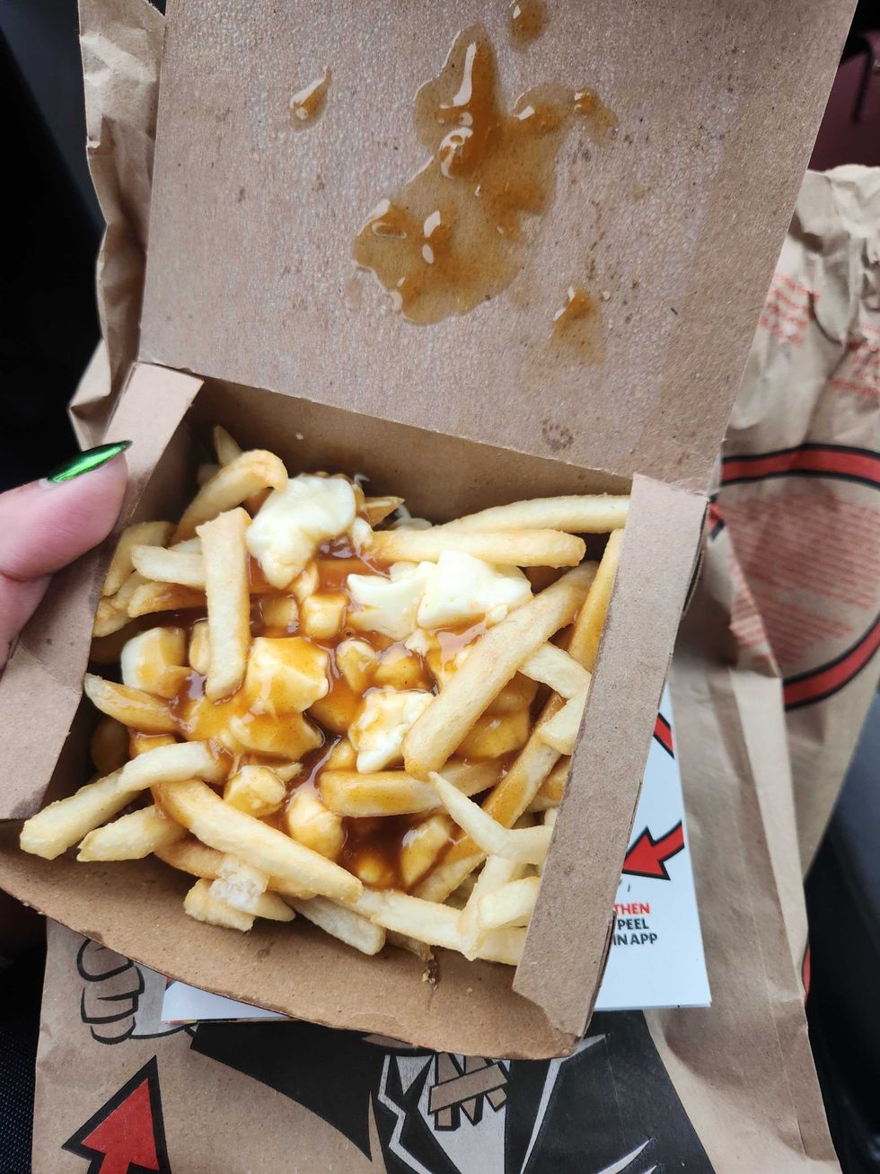A hand with green nail polish holding a brown box of poutine on top of a brown McDonald's bag.