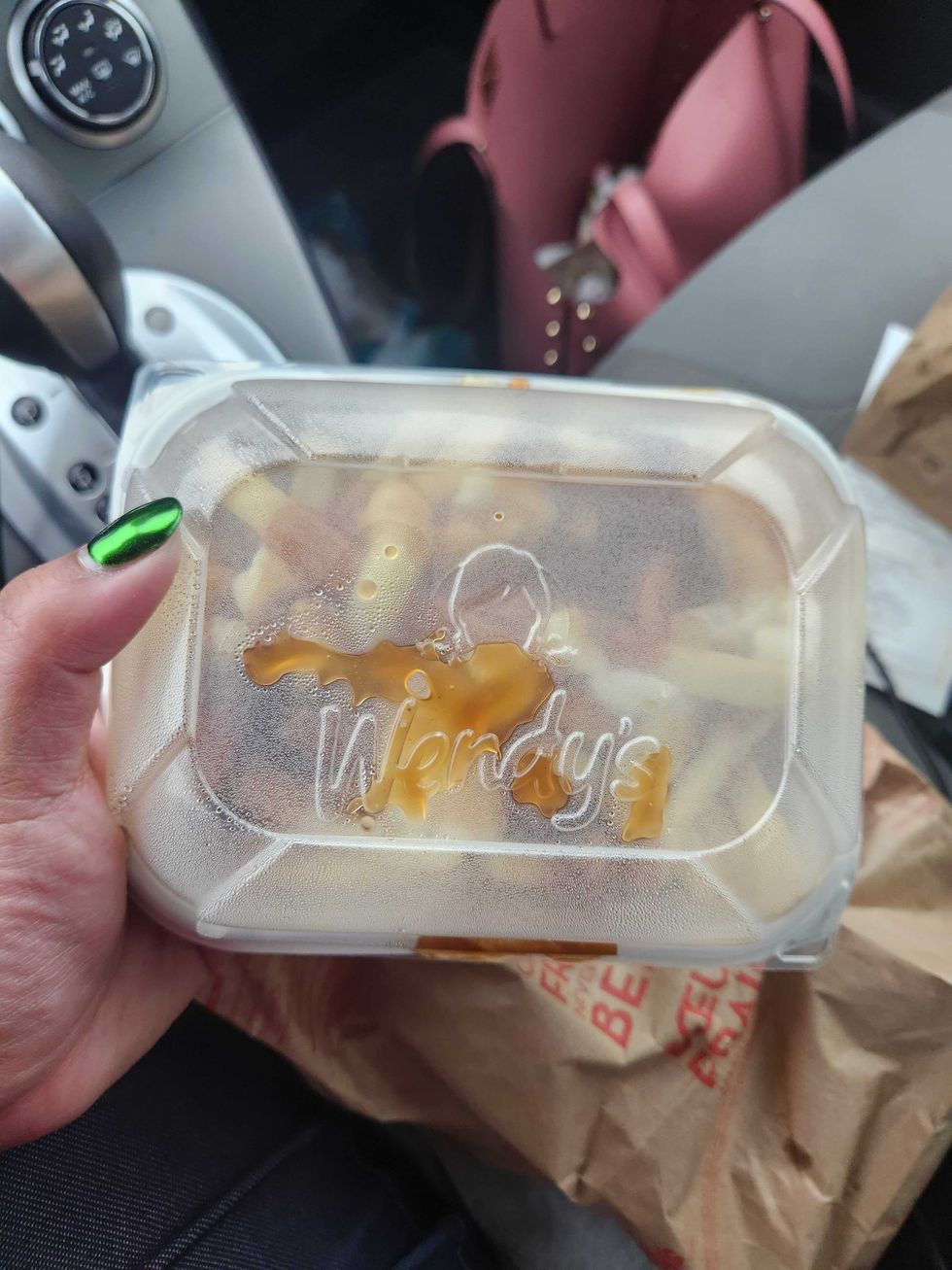 A hand with green nail polish holding a closed container of poutine with heat condensing on it that says Wendy's.