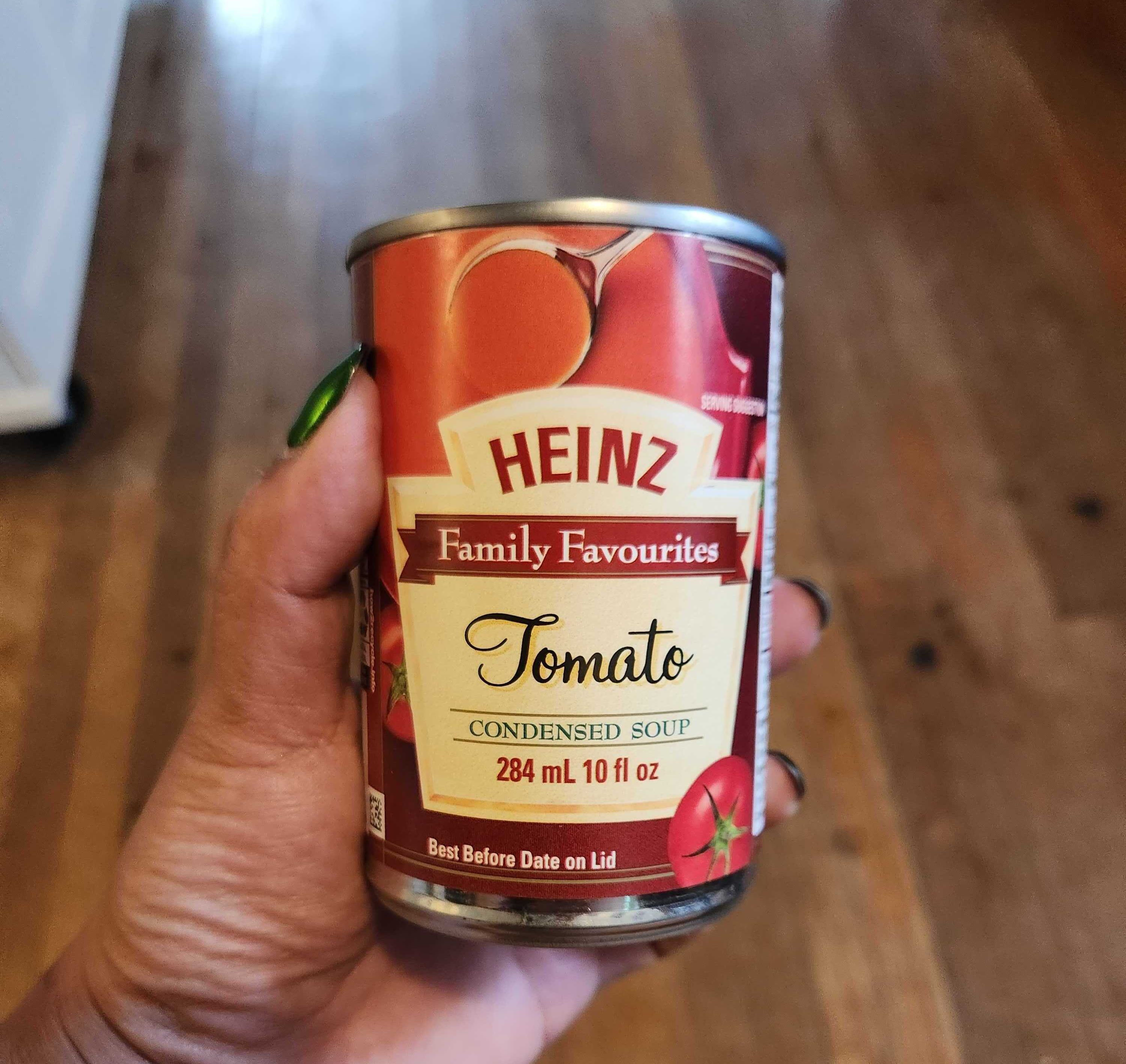 A hand with green nail polish holding a tin of soup.