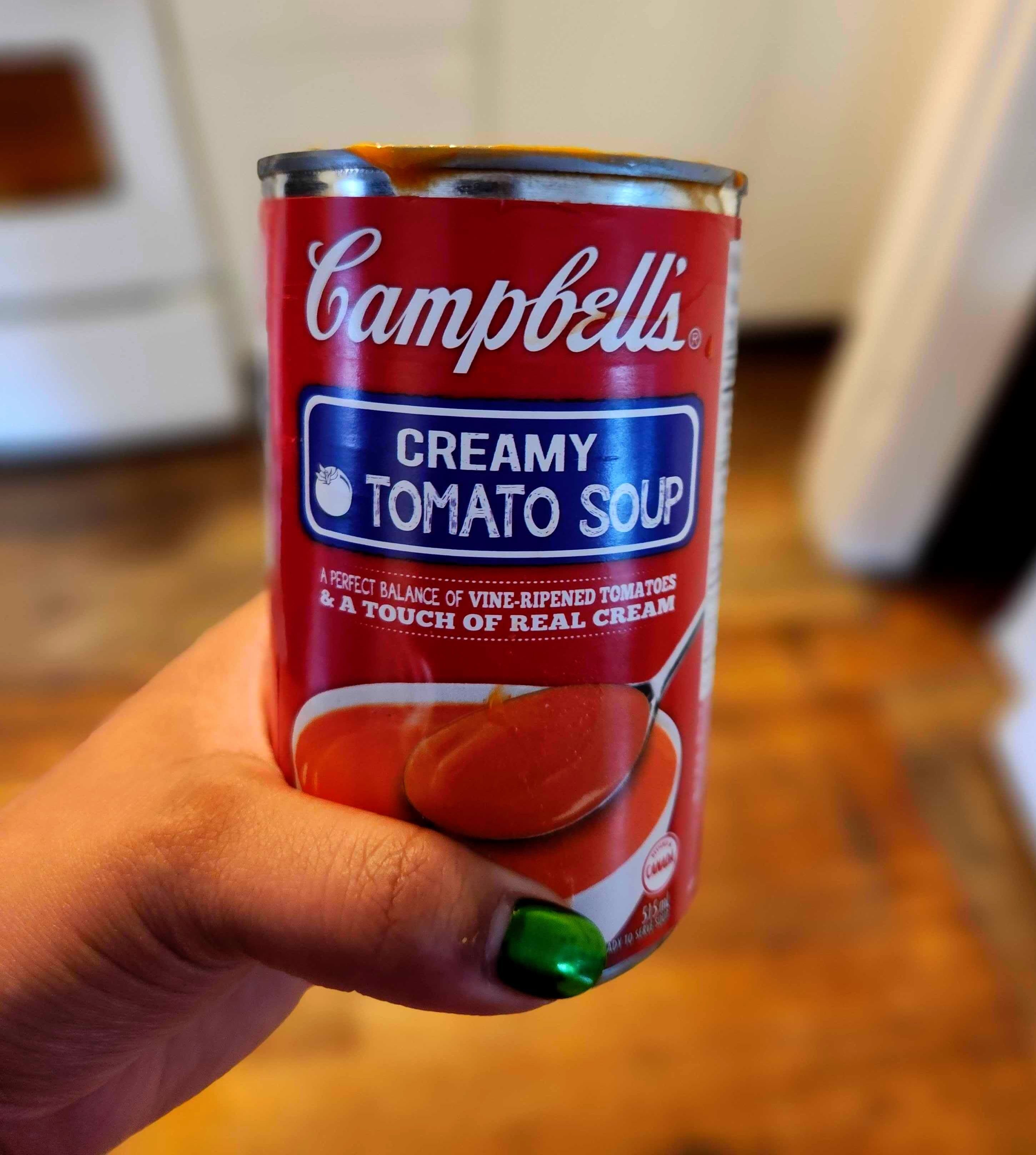 A hand with green nails holding a tin of soup.