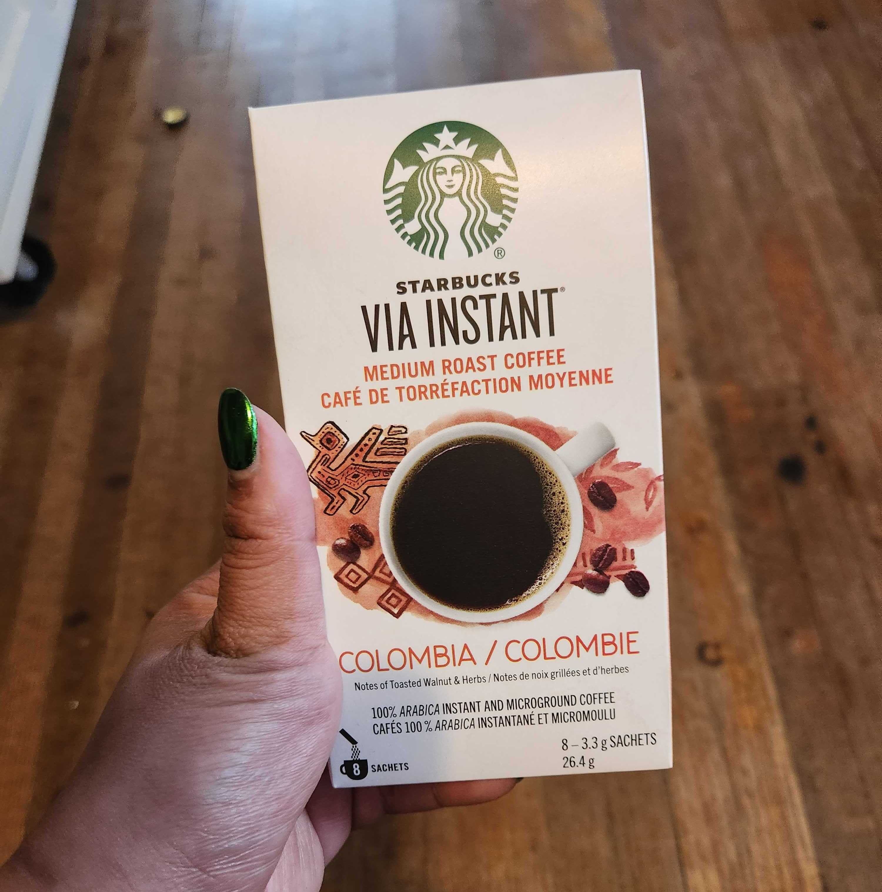 A hand with green nails holding a white package of coffee.