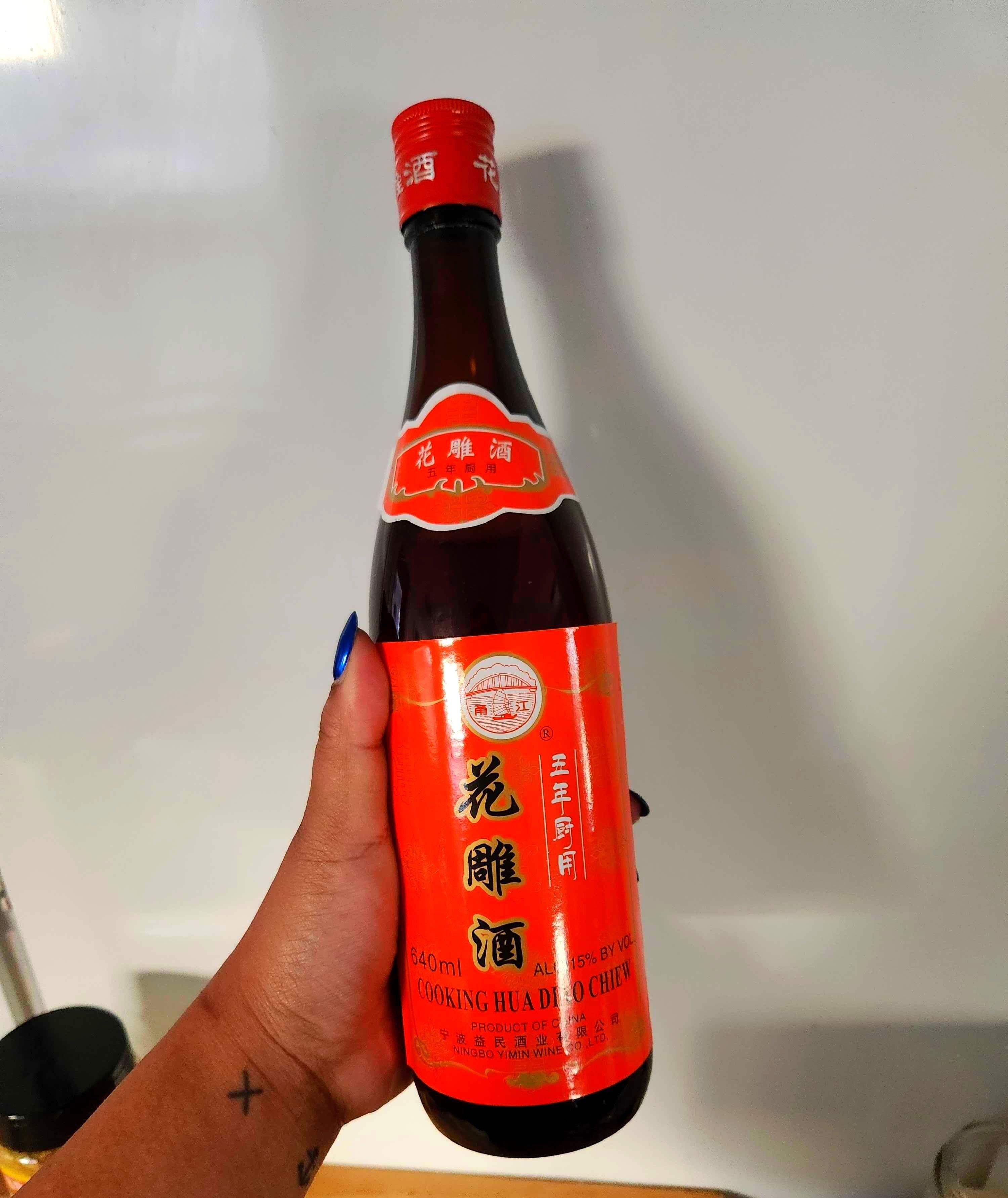 A hand with tattoos holding a orange and black bottle.