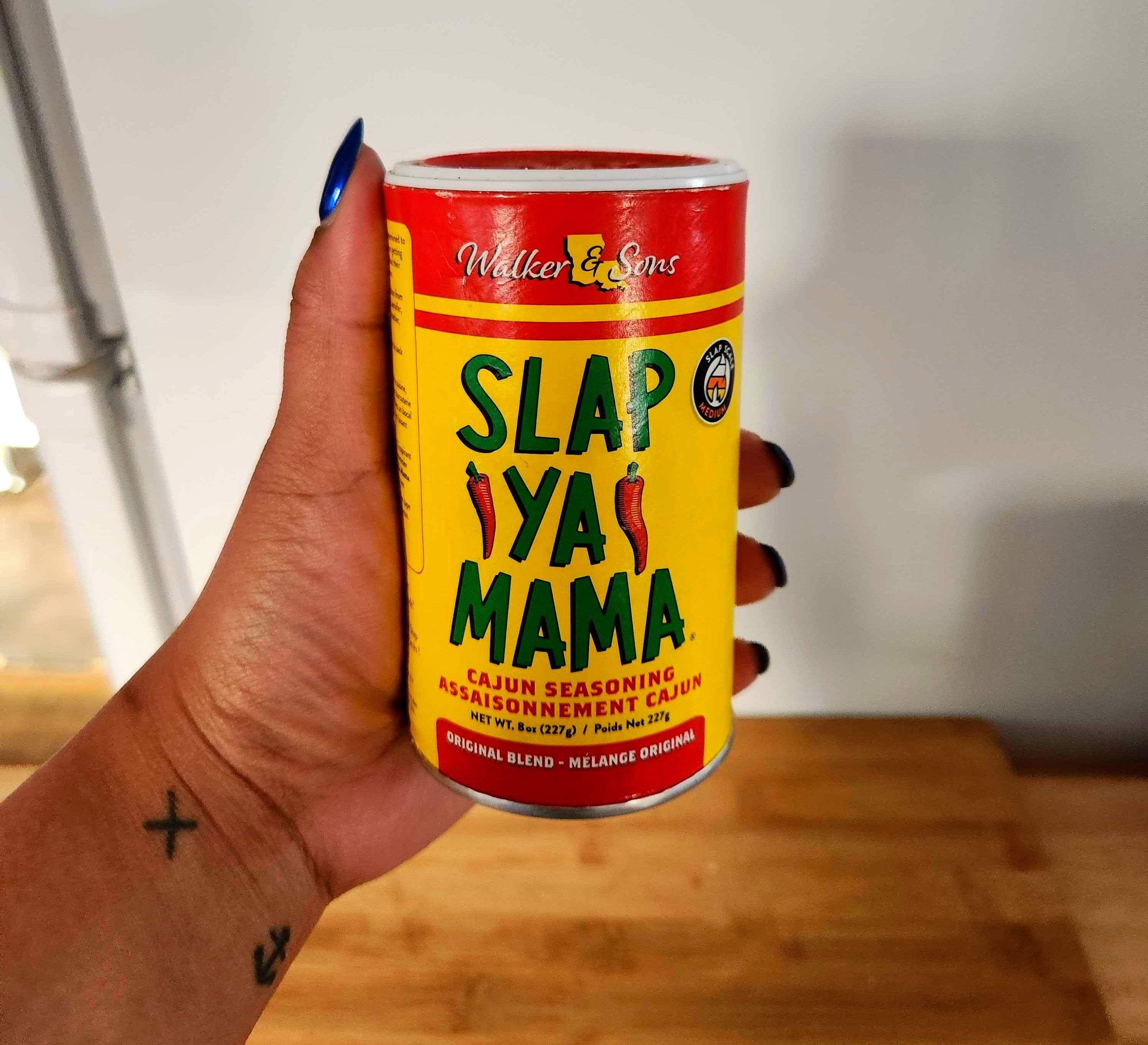 A hand with tattoos holding a red and yellow bottle.