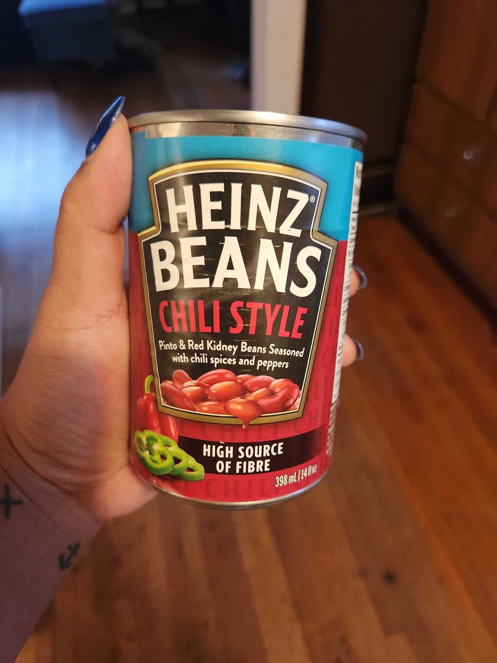 A hand with tattoos holding a tin with a red  and blue label against a brown floor.