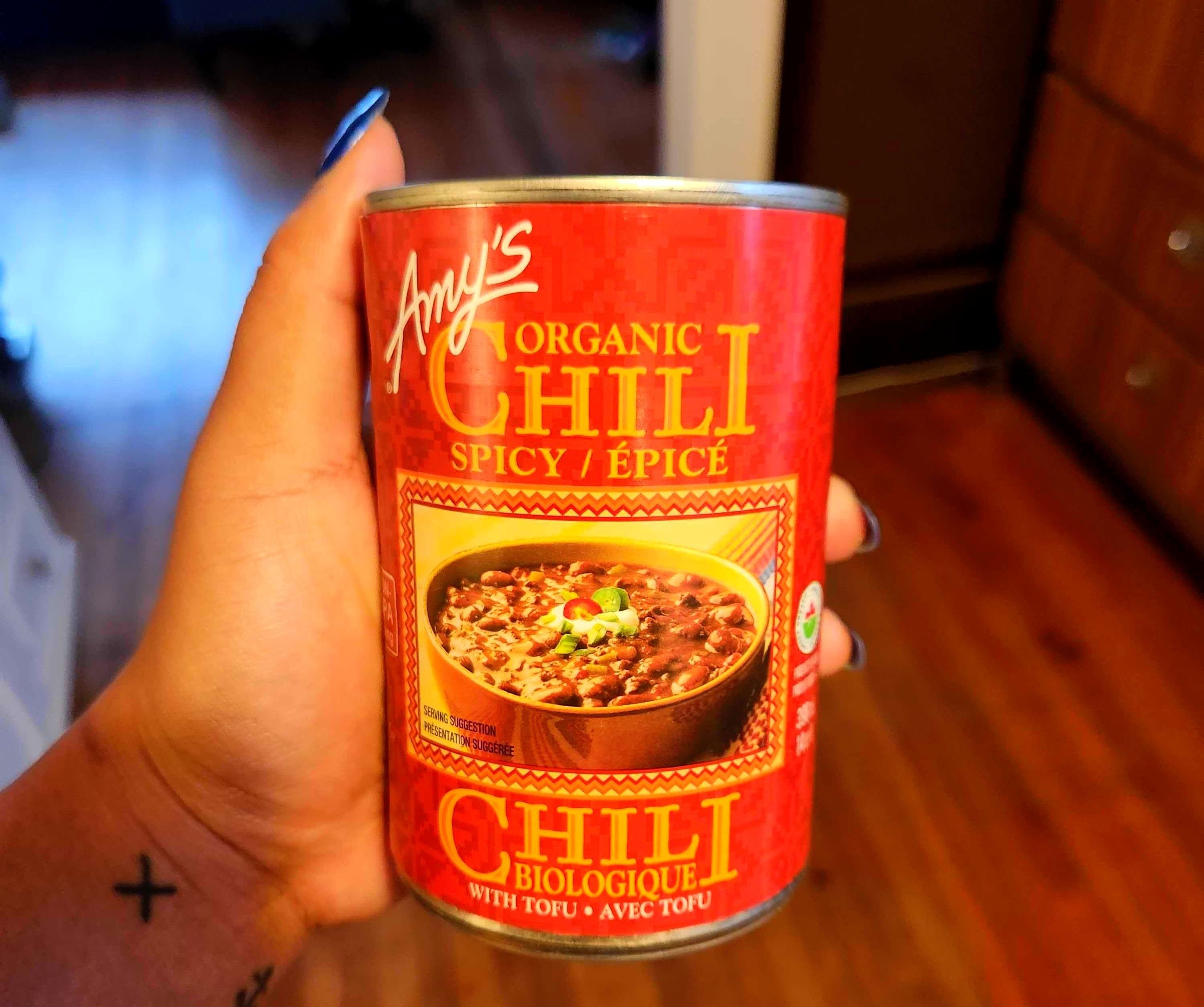 A hand with tattoos holding a tin with a red label against a brown floor.