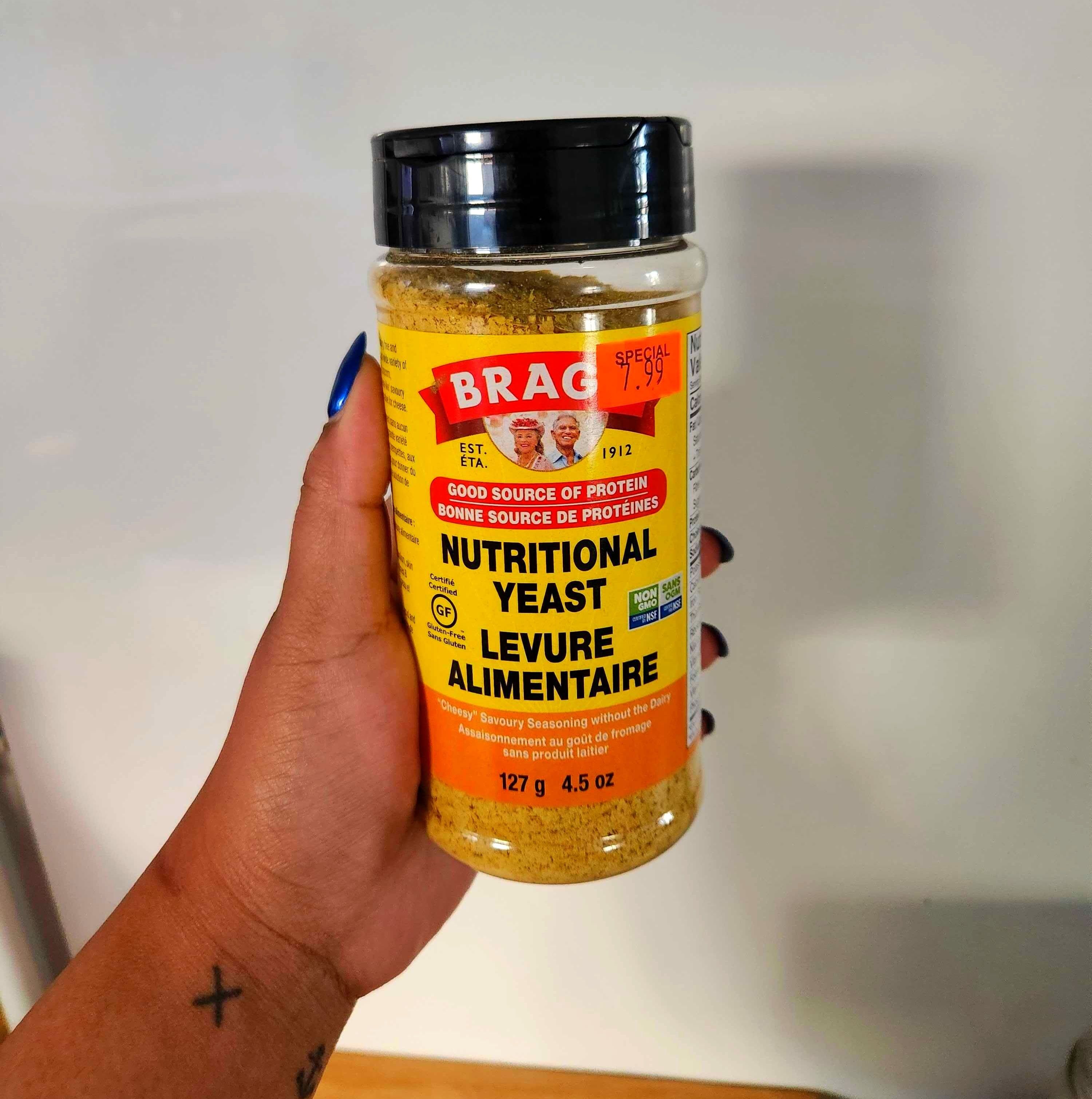 A hand with tattoos holding clear bottle with a yellow label.