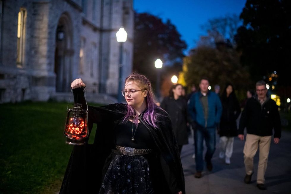 A Haunted Walk tour leader with purple hair wears a cloak and carries a lantern while leading ghost walk guests around Kingston, Ontario. 