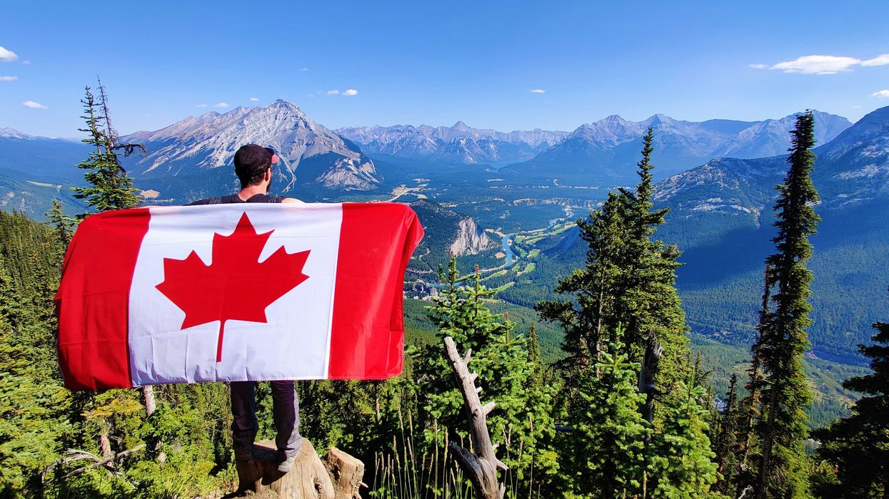 A hiker holding a Canada flag at a lookout over Banff (illustrative).