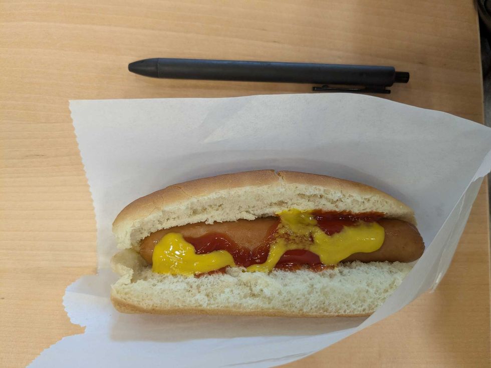 A hot dog with ketchup and mustard beside a pen for scale