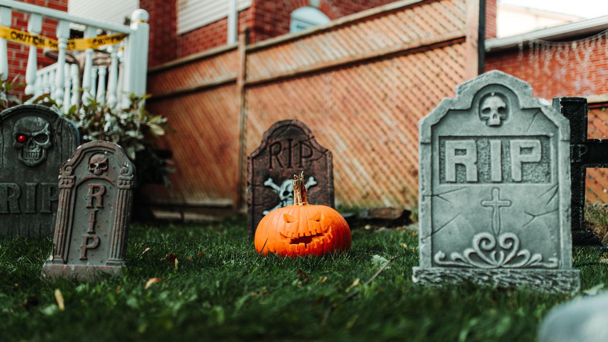 A jack-o'-lantern sits on a lawn surrounded by headstones.