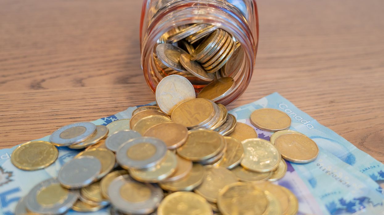 A jar filled with Canadian loonies and toonies, tipped on its side and spilling coins onto a table.