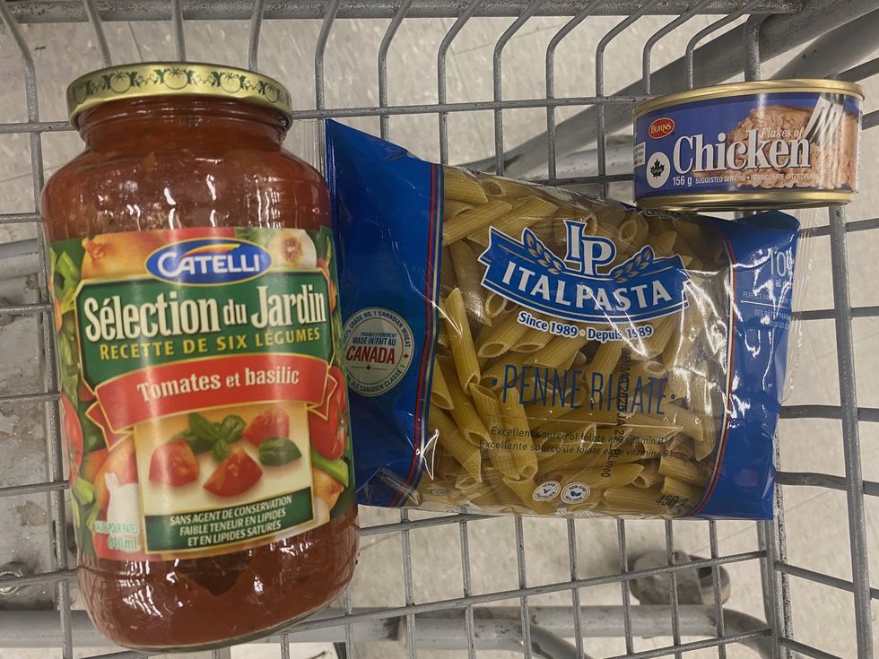 A jar of tomato sauce, a bag of penne pasta and a can of flaked chicken in a shopping cart.