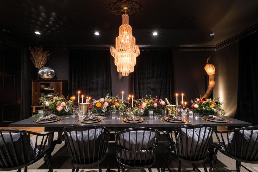 A large dining table complete with candles, flowers and a chandelier overhead.