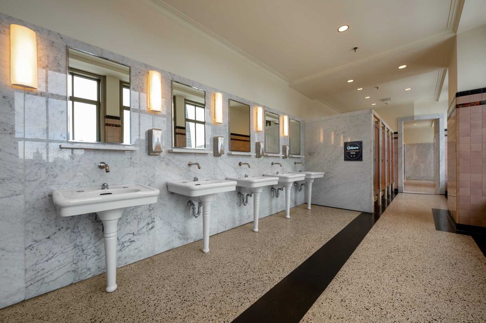 A large, elegant bathroom with stone floor, marble walls and white basins.