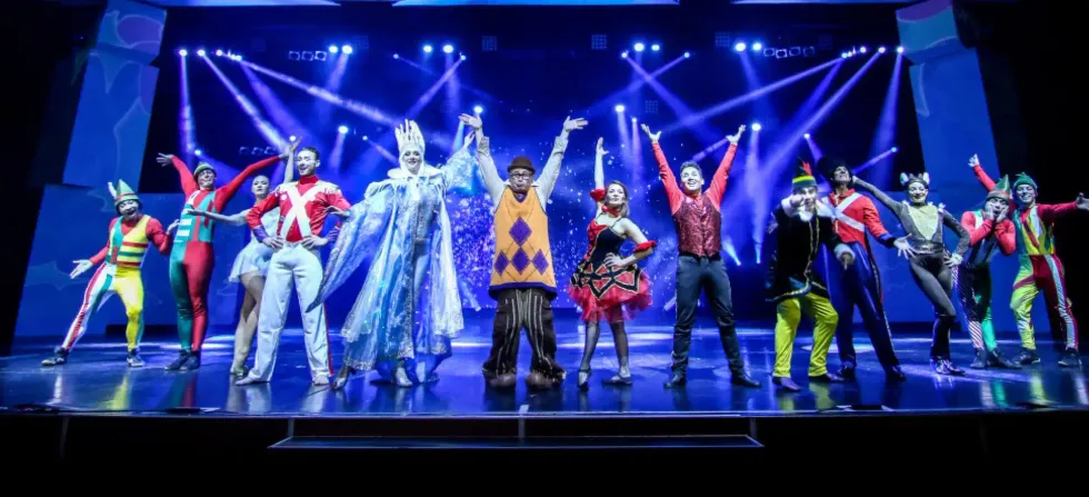 A large ensemble of costumed performers takes a bow on a brightly lit stage