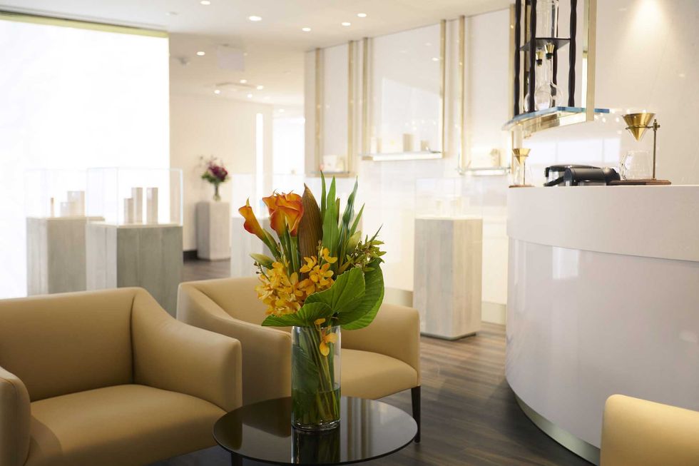 A light-filled waiting room with yellow chairs, flowers in a vase and a white reception desk.