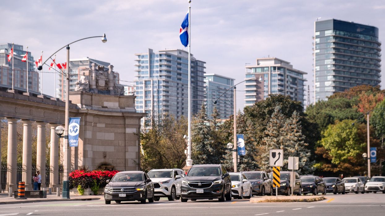 A line of cars at a traffic light on Strachan Avenue at Lake Shore Boulevard in Toronto with high-rises of the King West Village neighborhood in the background.