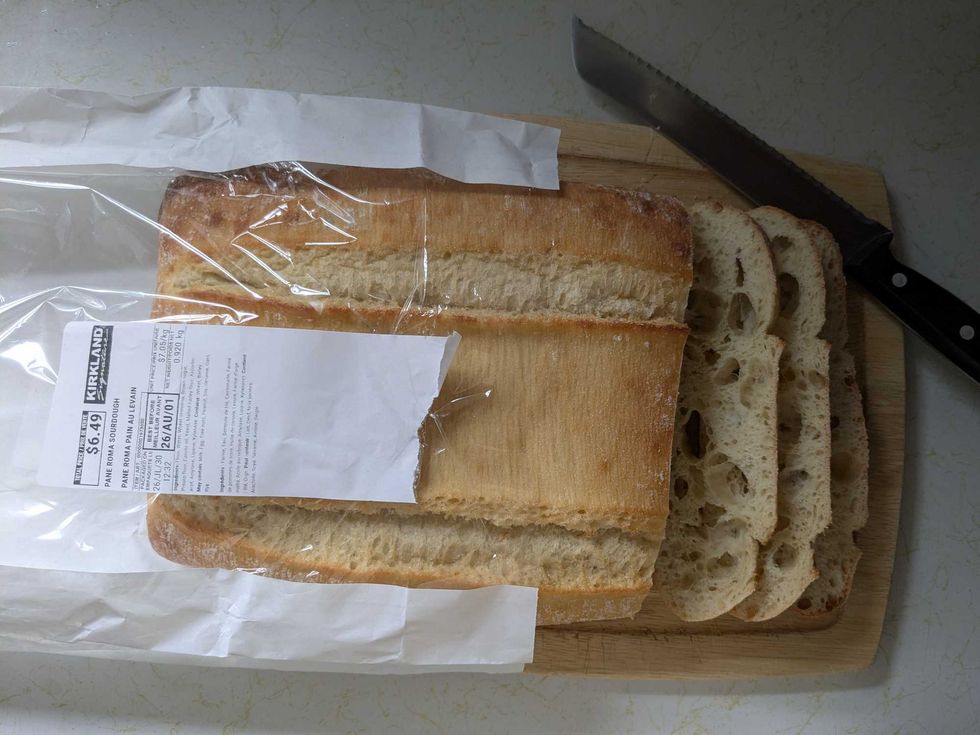 A loaf of Costco sourdough bread on a cutting board with a few slices cut beside a knife