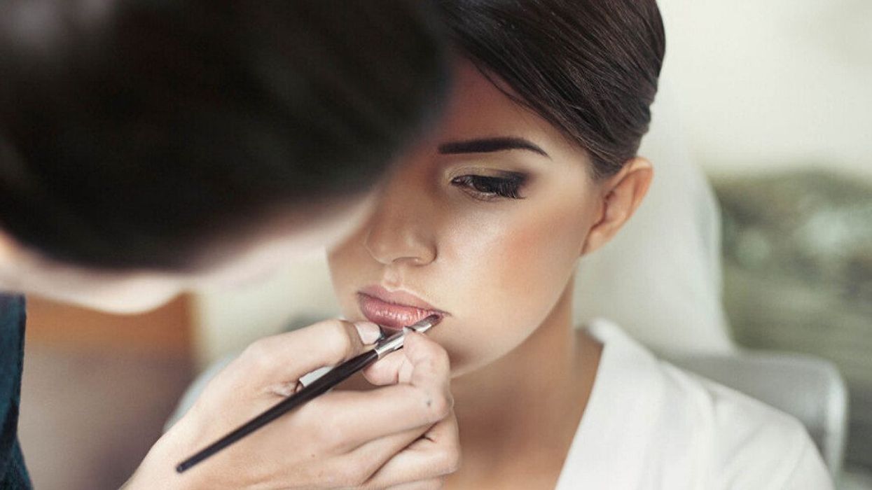 A makeup artist applying makeup to a bride's face on her wedding day.