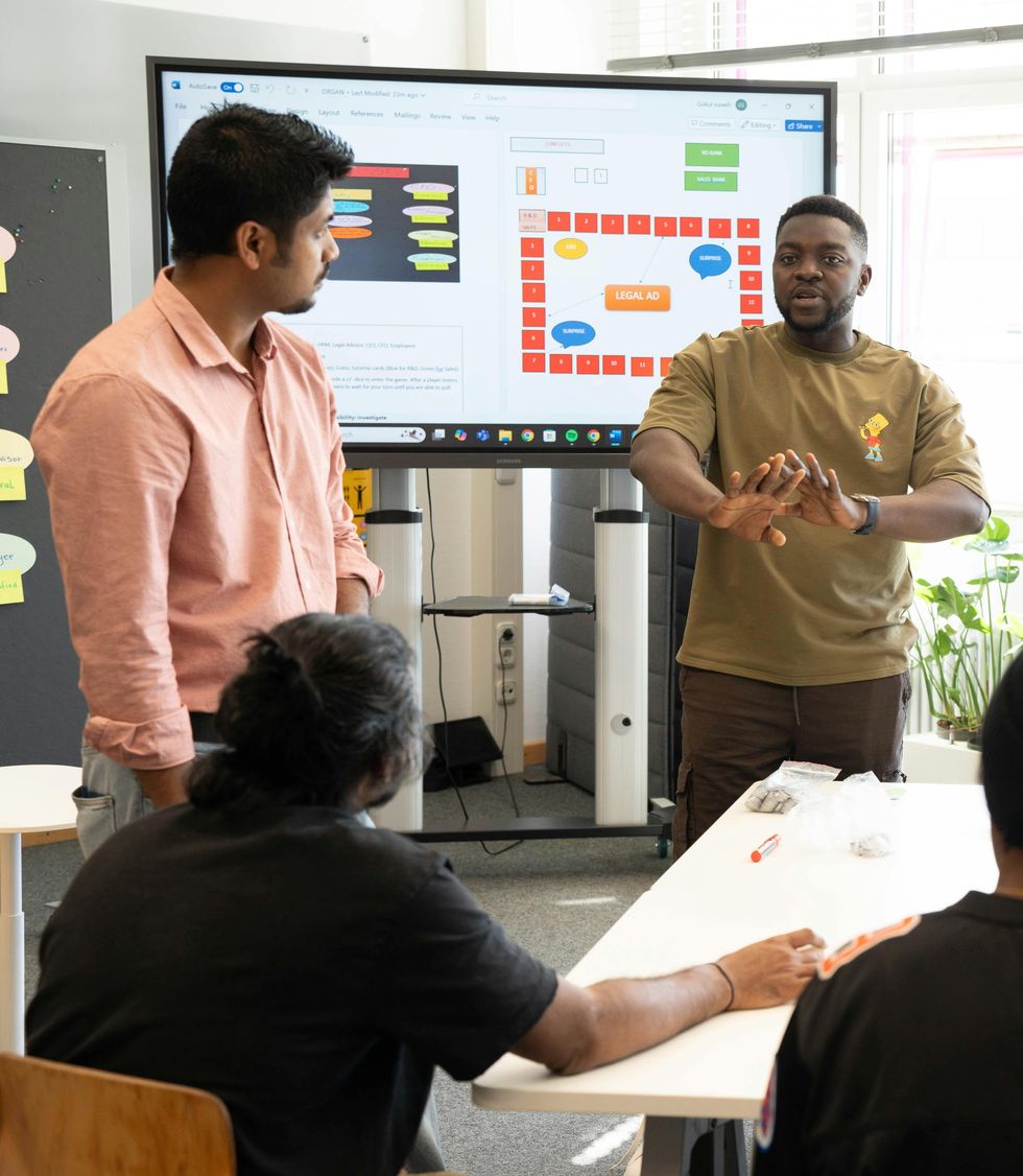 A man delivering a presentation in an office in front of a TV displaying a flowchart.