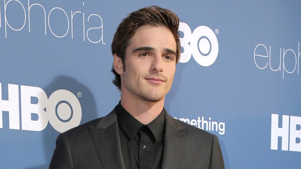 A man in a black suit smiling at the camera with works like "Euphoria" and "HBO" behind him.