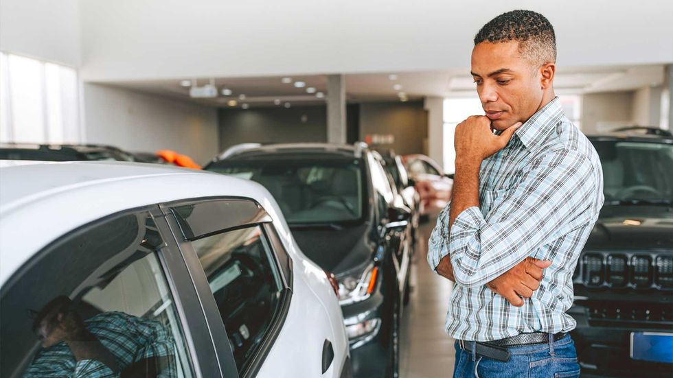 A man in a blue shirt looks at a used car in a dealership.