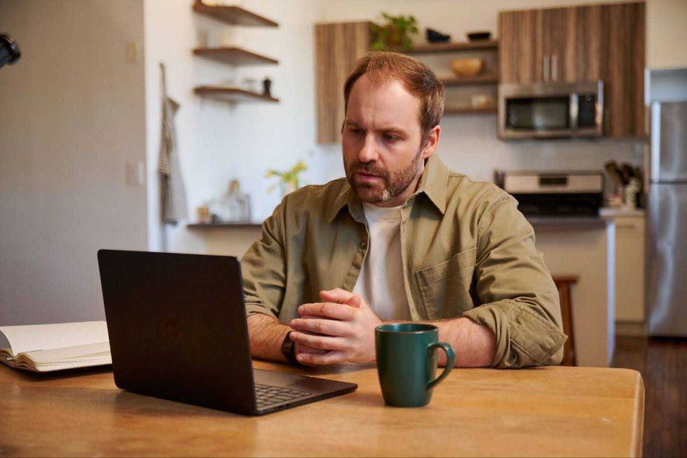 A man in a khaki shirt speaks with someone over video chat.