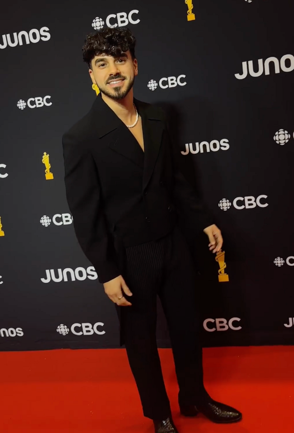 A man in an all-black suit posing for a photo on a red carpet.