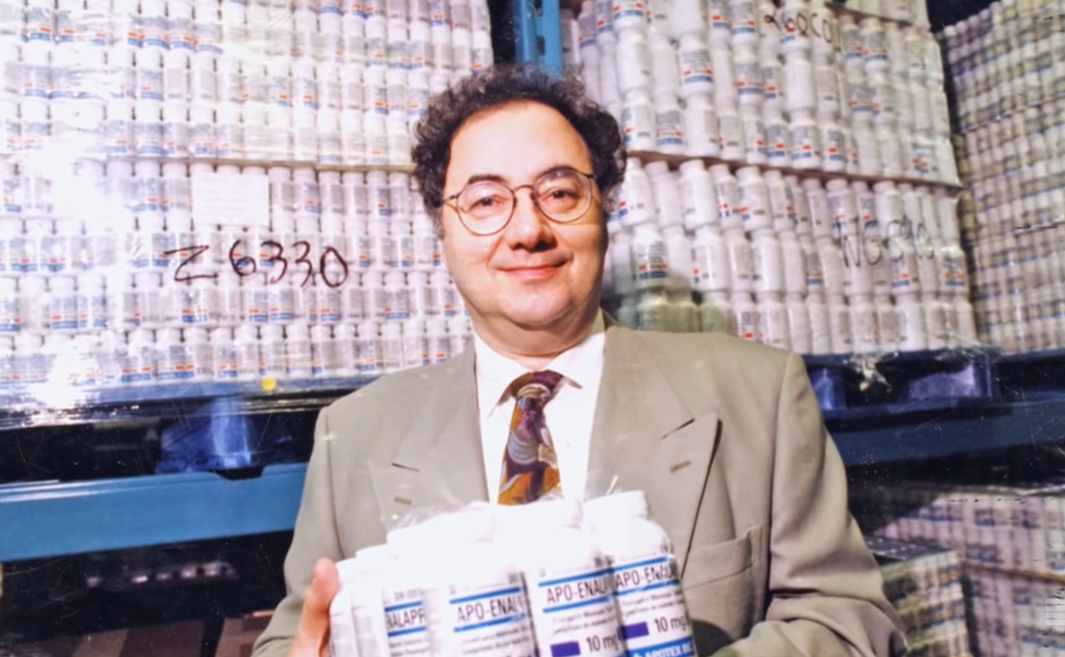 A man in glasses posing for a photo in front of and holding several bottles of pills.