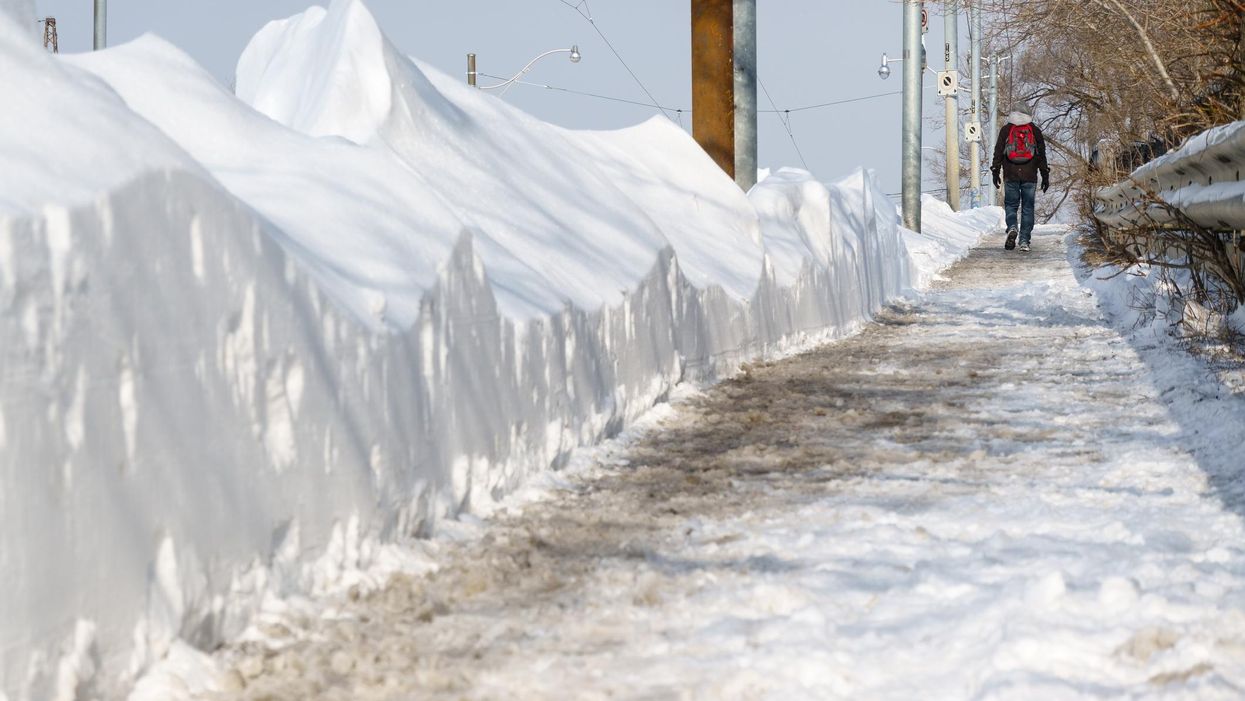 A man walks on a snowy sidewalk in Toronto.
