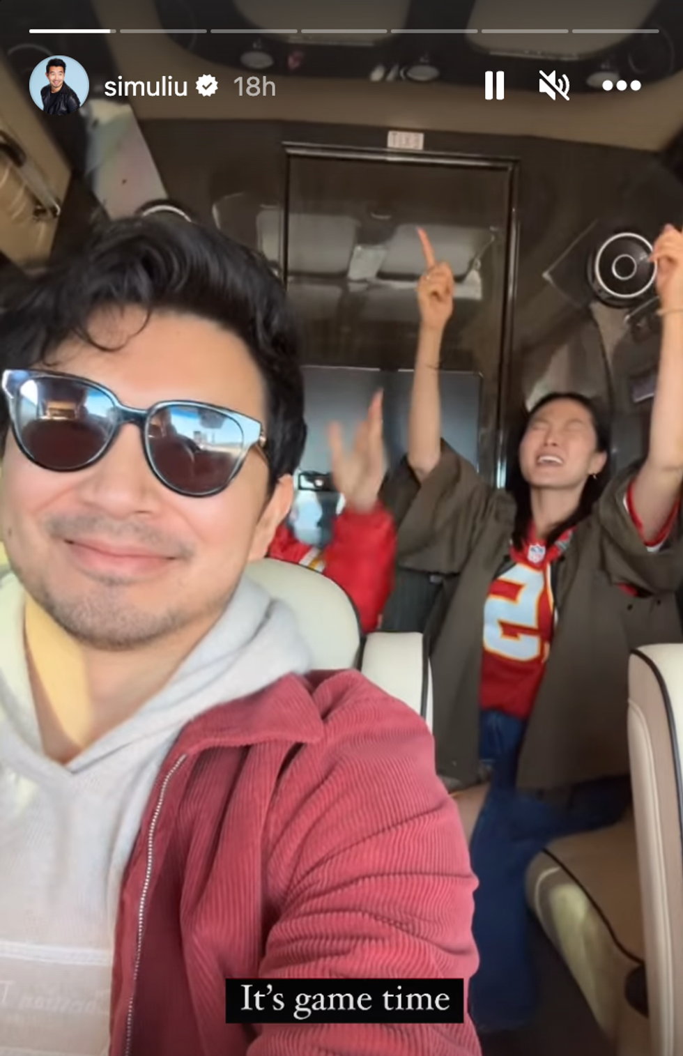 A man wearing sunglasses taking a selfie with a woman singing behind him.