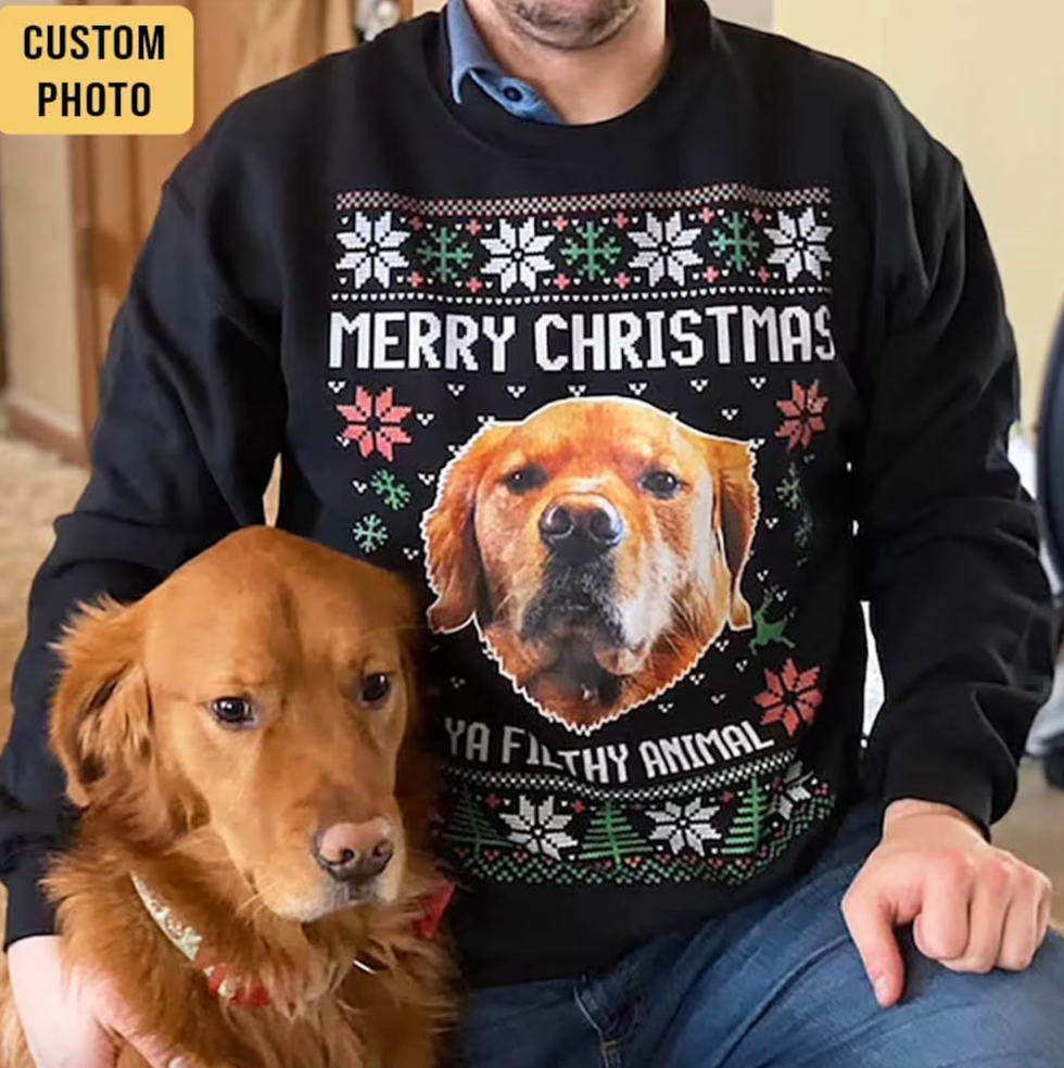 A man with a photo of his dog's face on it and text that says "Merry Christmas, Ya Filthy Animal" and his dog sitting next to him.