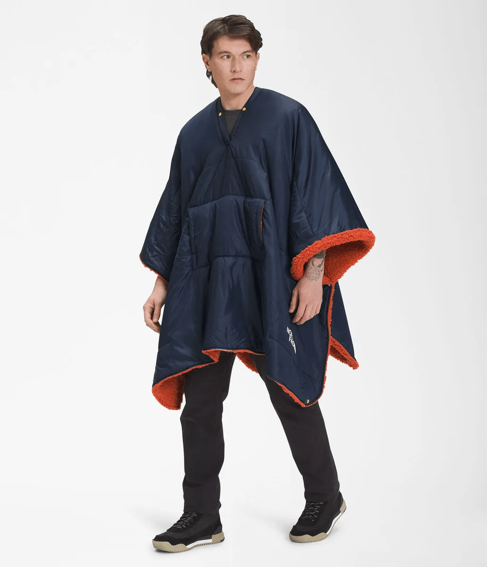 A man with dark hair models a navy poncho with fuzzy red lining.