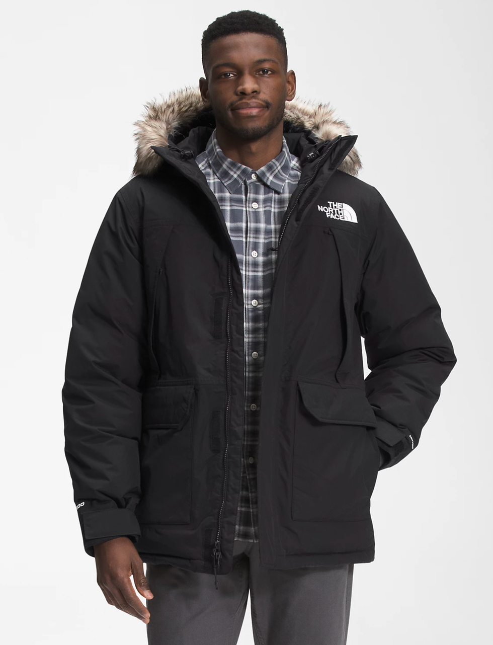 A model wearing a black winter jacket with a plaid shirt underneath and grey pants.