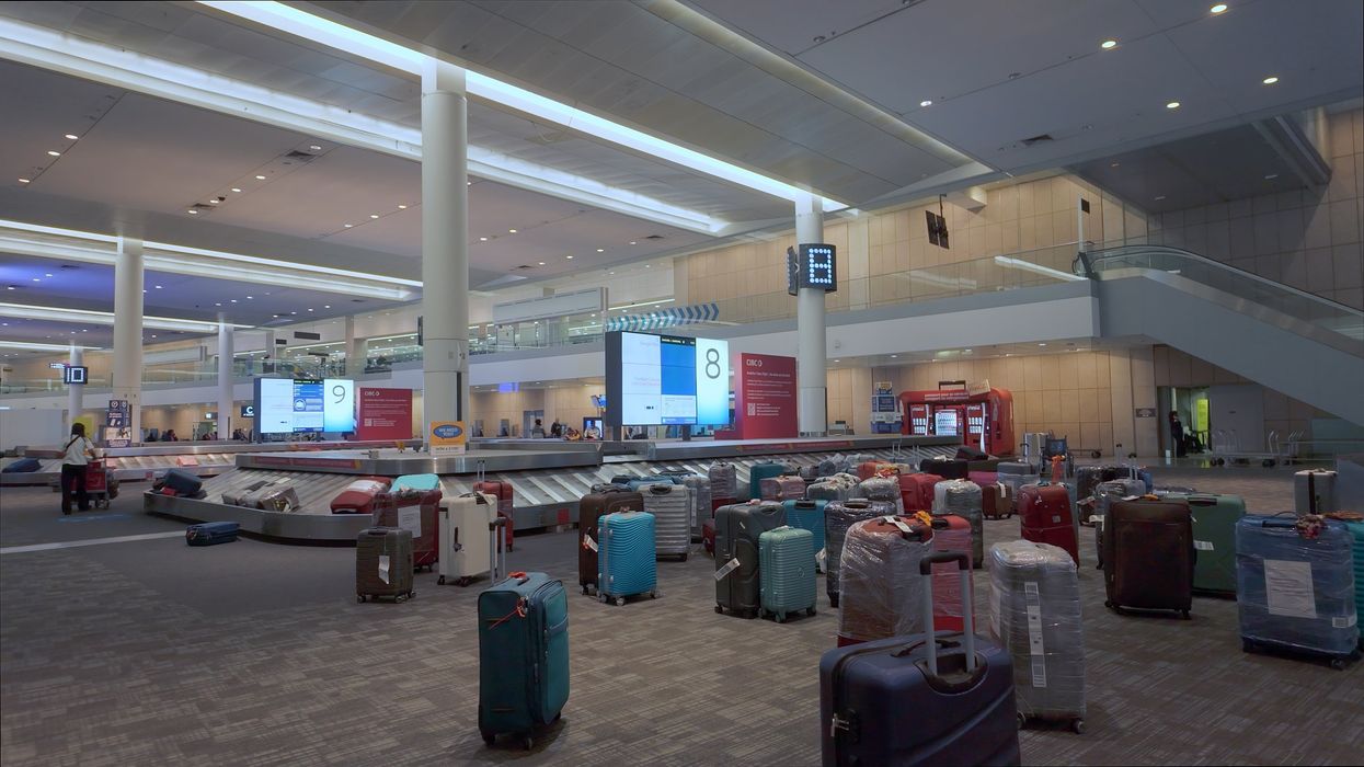 A modern airport baggage claim area with multiple carousels, suitcases scattered on the floor, and digital signage displaying carousel numbers.