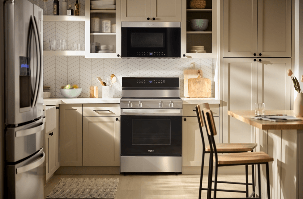 A modern kitchen featuring a stainless steel oven, range, and microwave with neutral cabinetry, open shelving, and a bright, airy design.