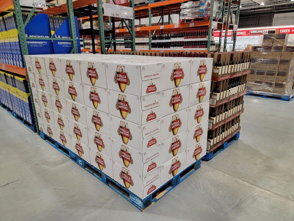 A pallet of Stella Artois beer cases stacked in the Brantford Costco, positioned next to other alcoholic beverages and bulk items in the warehouse aisle.