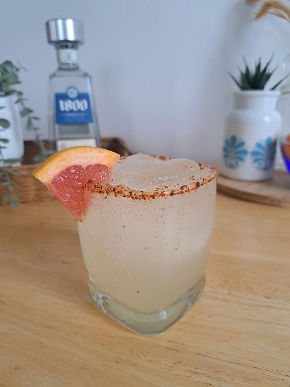 A paloma cocktail in a rocks glass, rimmed with Tajin and garnished with a wedge of grapefruit.