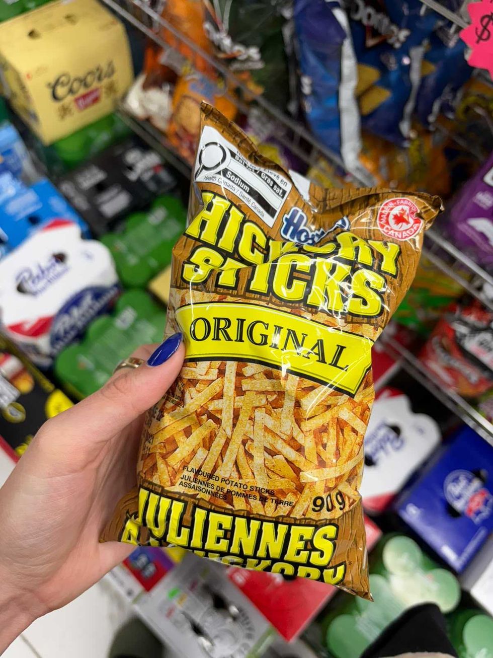 A person holding a bag of Hickory Sticks in a grocery store.