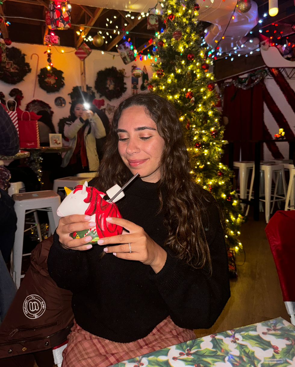 A person holding a drink in a unicorn mug in a Christmas pop-up bar.