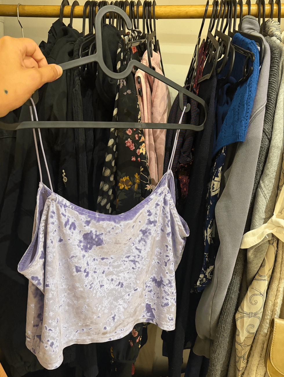 A person holding a shirt in front of other hanging clothing.