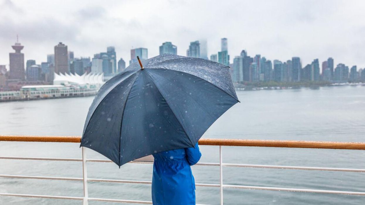 A person holding an umbrella looking at the Vancouver skyline in the rain.