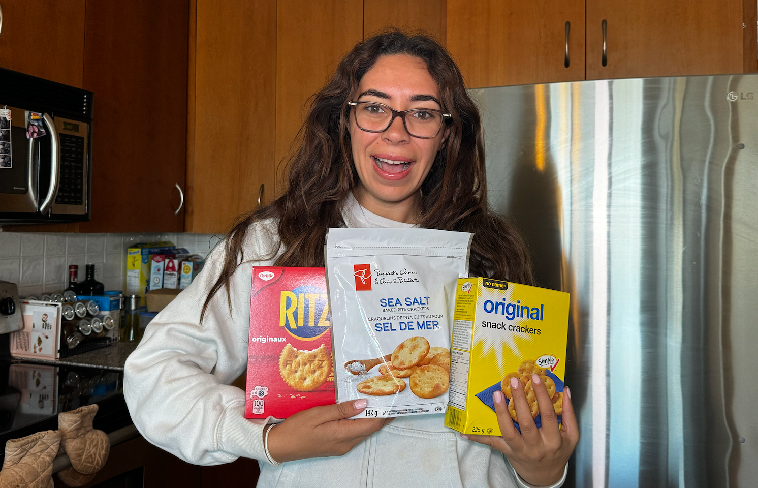 A person holding three crackers brands, RITZ, President's Choice and no name.