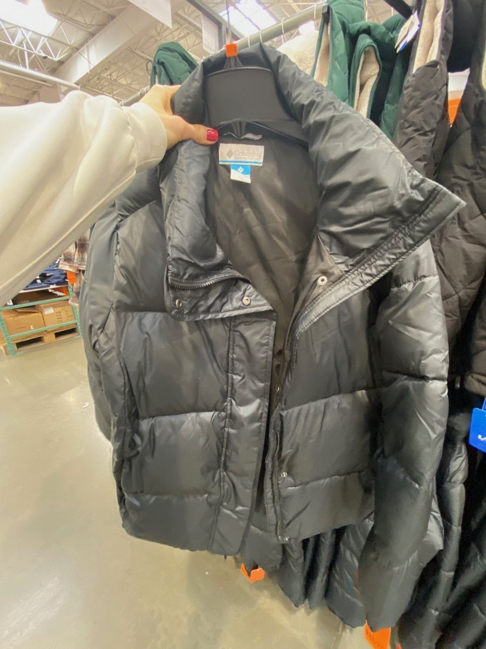 A person holding up a black jacket at Costco.
