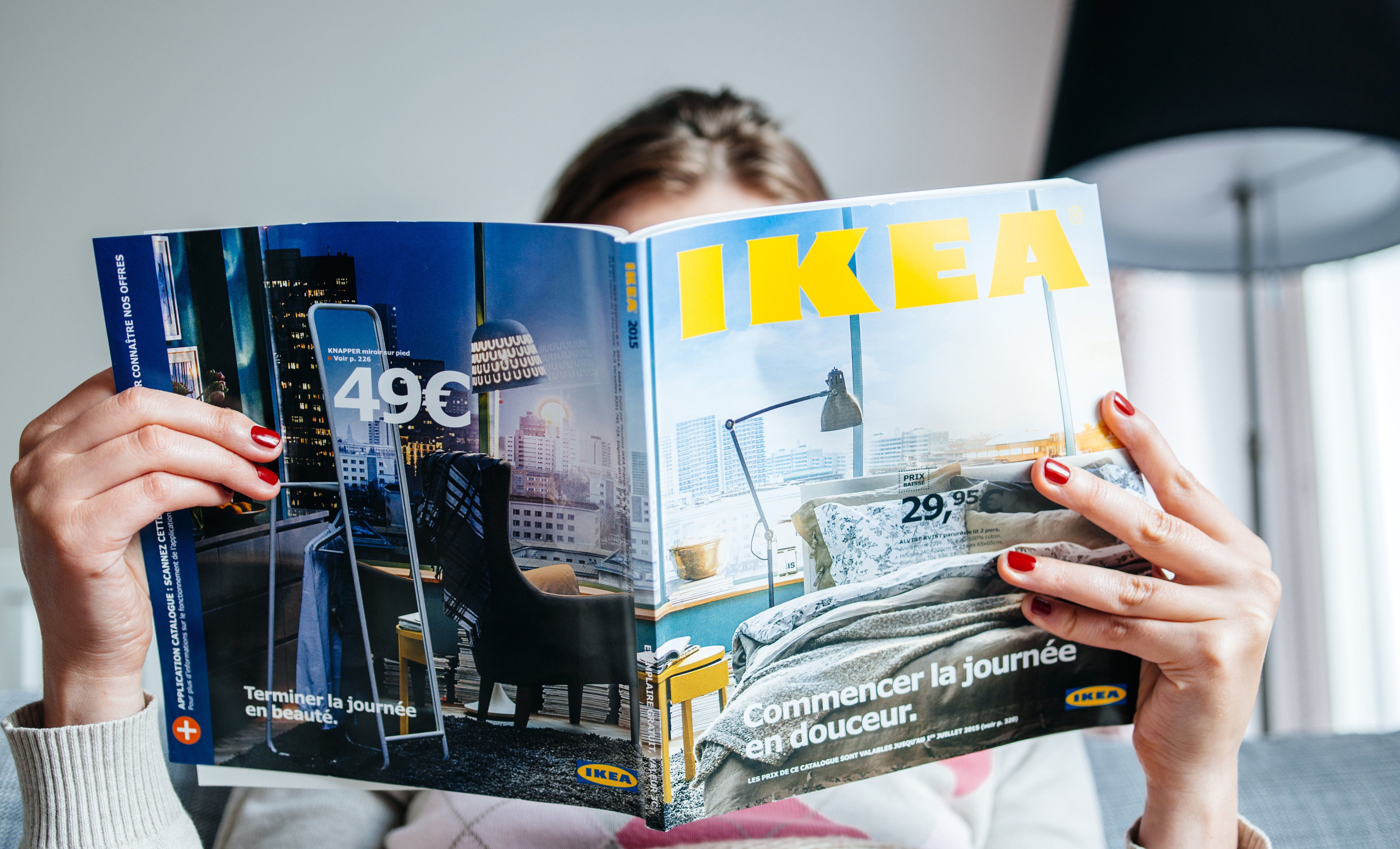A person holding up an IKEA catalogue and reading it while sitting down.