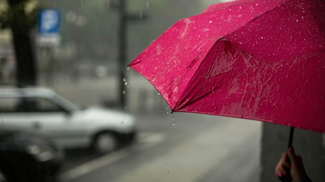 A person holds a red umbrella outside while it rains.