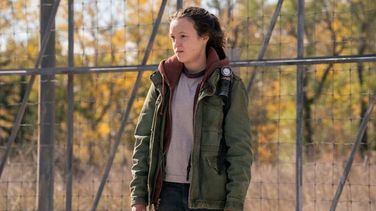 A person in a t-shirt, maroon zip-up sweater and khaki green jacket looking off camera.